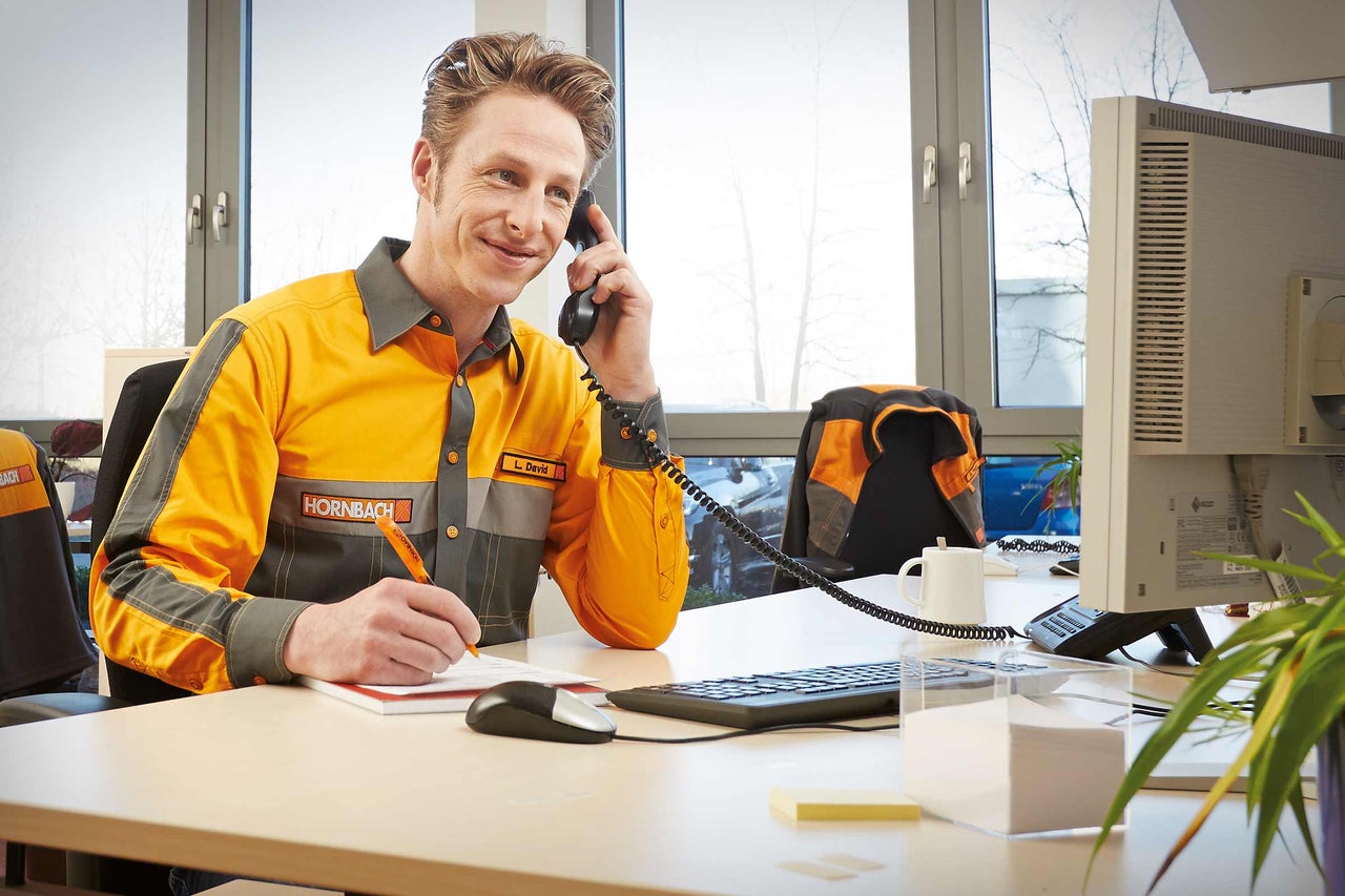 Een Hornbach medewerker telefoneert en maakt aantekeningen aan zijn bureau.
