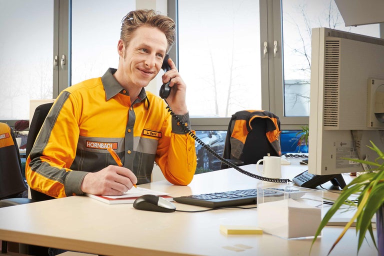 Een Hornbach medewerker telefoneert en maakt aantekeningen aan zijn bureau.