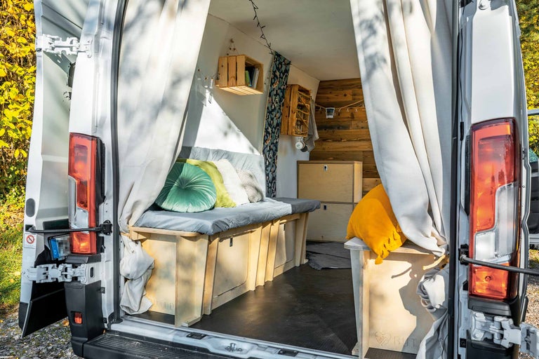 Interieur van een omgebouwde bestelwagen met houten elementen, opbergruimte onder het bed en gordijnen