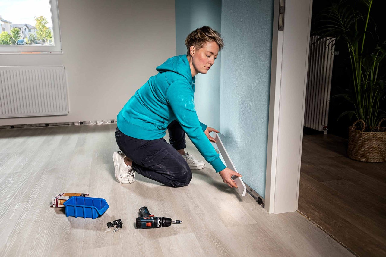 Vrouw bevestigt plint aan de muur in een kamer met laminaatvloer