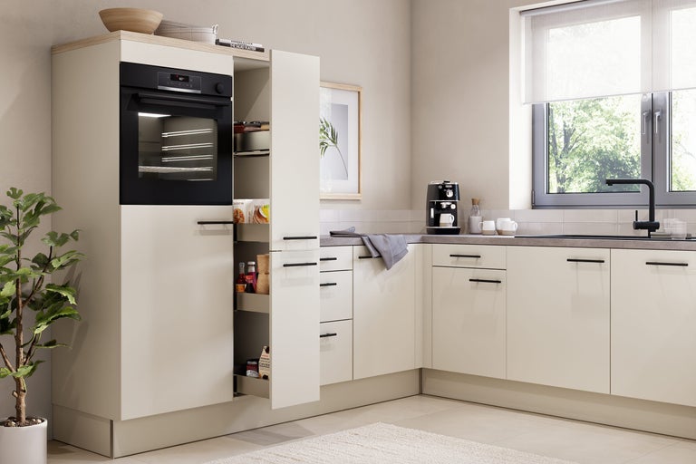 Moderne L-vormige keuken in beige met zwarte inbouwoven, apothekerskast, grijs werkblad en zwarte kraan bij het raam.