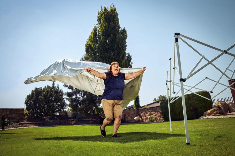 Een vrouw in de tuin houdt een tentzeil omhoog, naast een paviljoen.