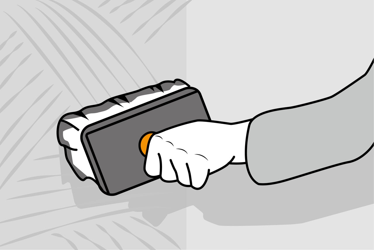 Hand die een schuurblok op een muur aanbrengt