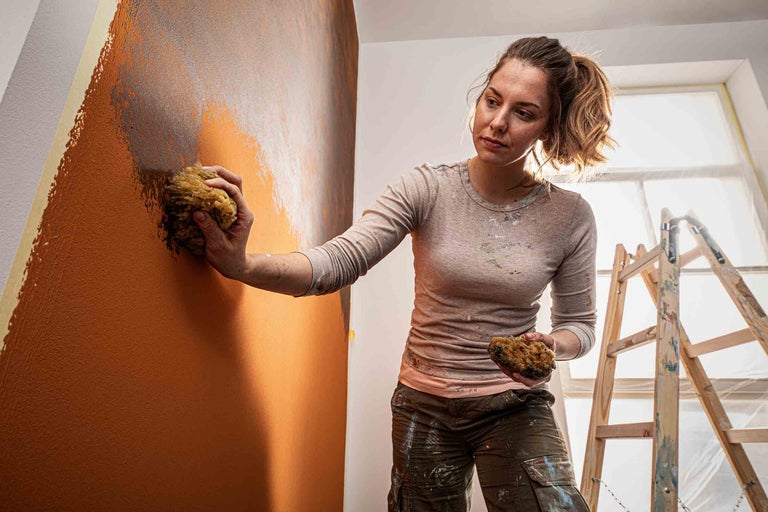 Vrouw decoreert muur met spons en verf, inclusief ladder in de ruimte