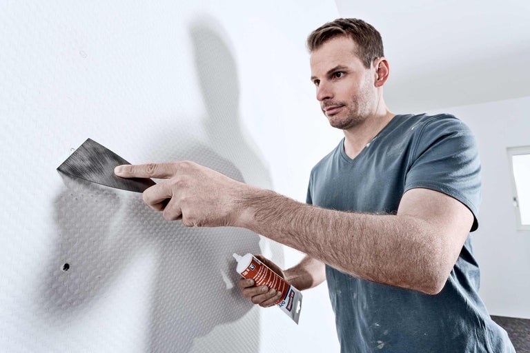 Een man vult een gat in een muur met vulmiddel en een plamuurmes