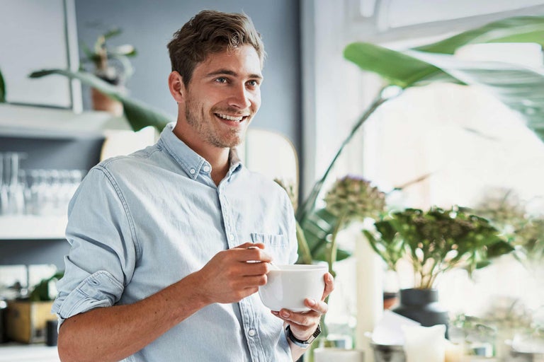 Lachende man met een kom ontbijtgranen in een lichte keuken met planten