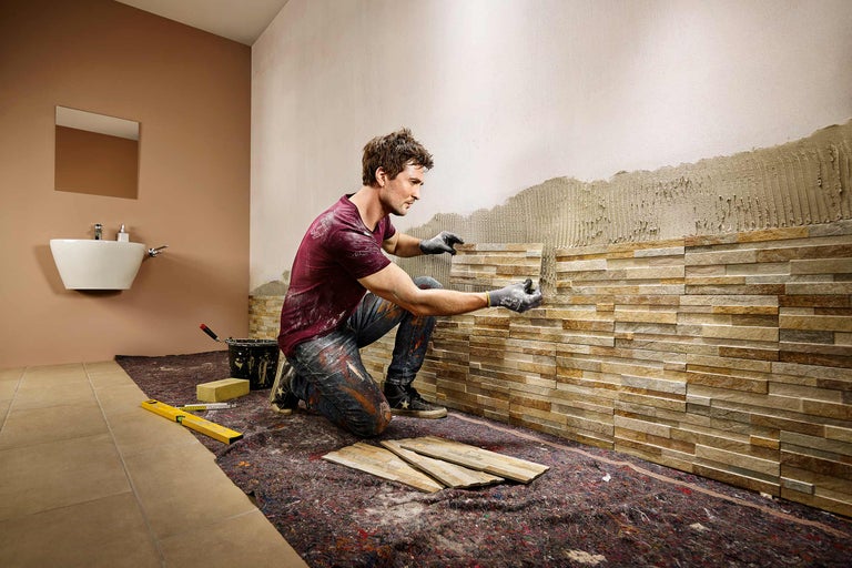 Man installeert natuurstenen wandbekleding in de badkamer.