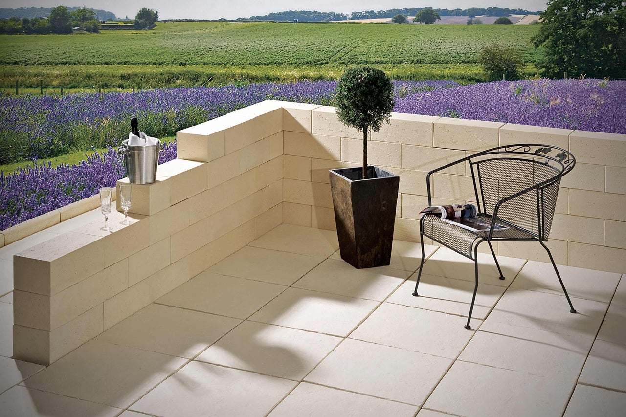 Terras met stenen tegels, muur, plant in pot en tuinstoel