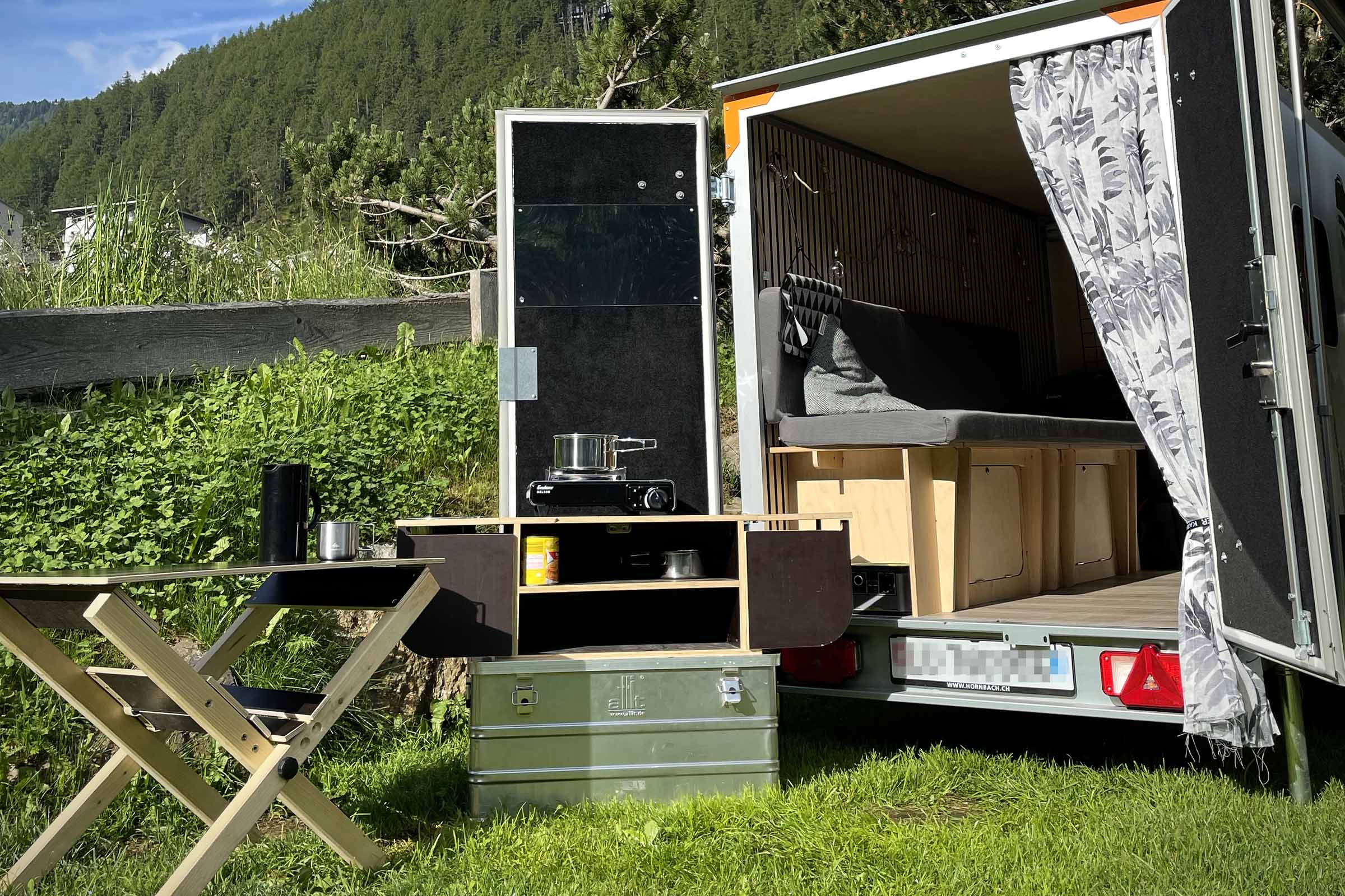 Kampeeraanhanger met keuken, tafel en opbergruimte in de buitenlucht.