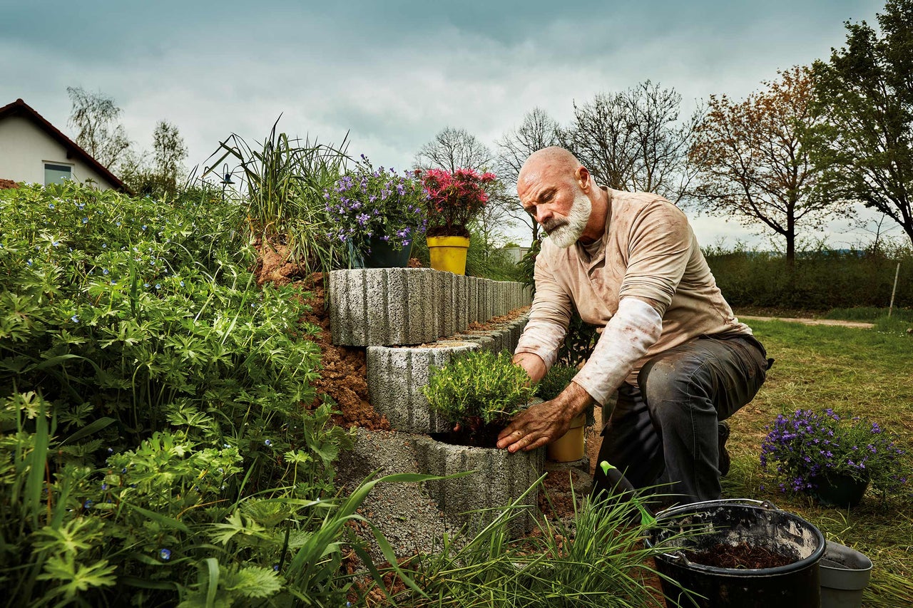Een man beplant een tuinmuur van betonblokken met planten.