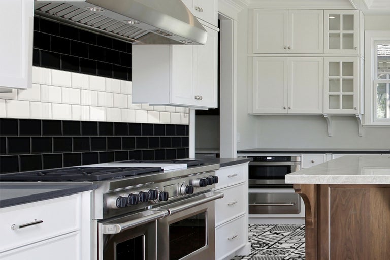 Lichte keuken met aanrecht, afzuigkap, fornuis, witte kasten en tegels in zwart en wit