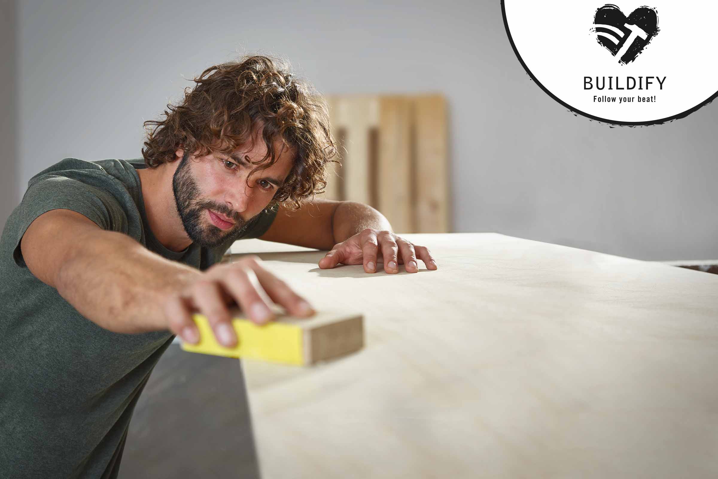 Een man schuurt hout met een schuurblok. Buildify Logo.