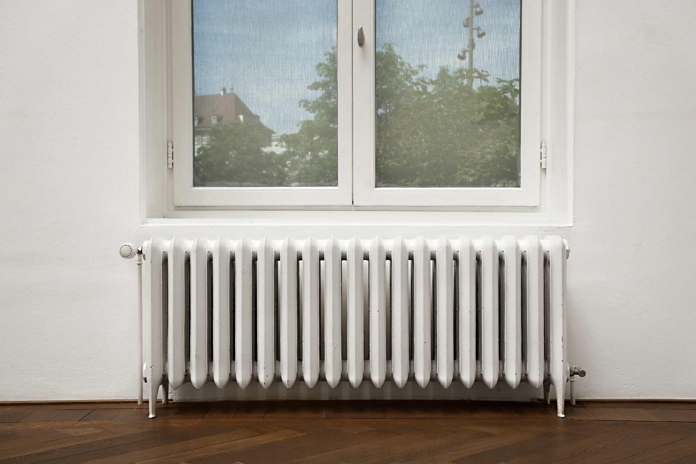 Witte radiator onder een raam op een houten vloer