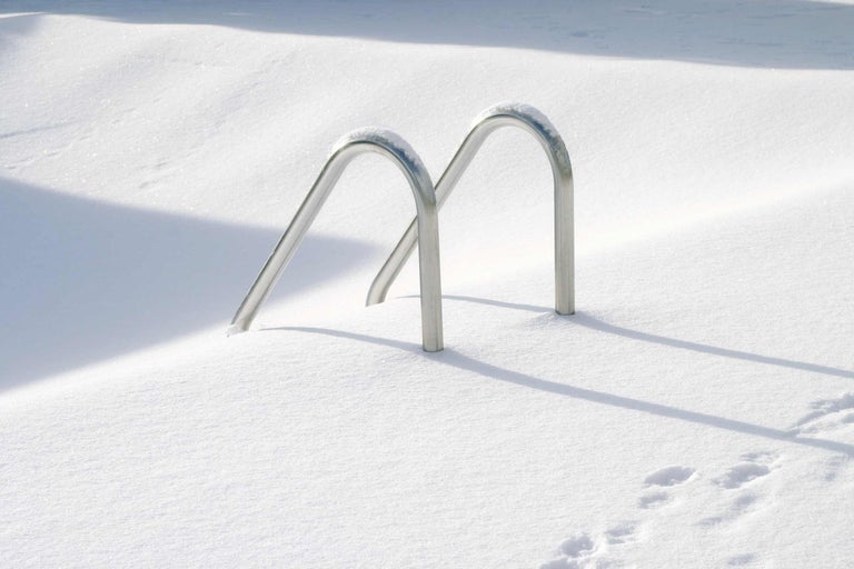 Een metalen zwembadladder is in de sneeuw verzonken.
