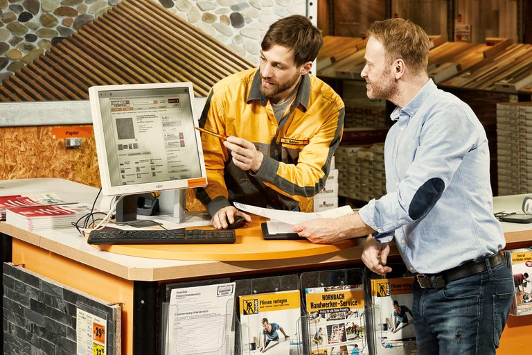 Twee medewerkers overleggen bij een adviestafel bij Hornbach, waarop een computer staat met de Hornbach website.