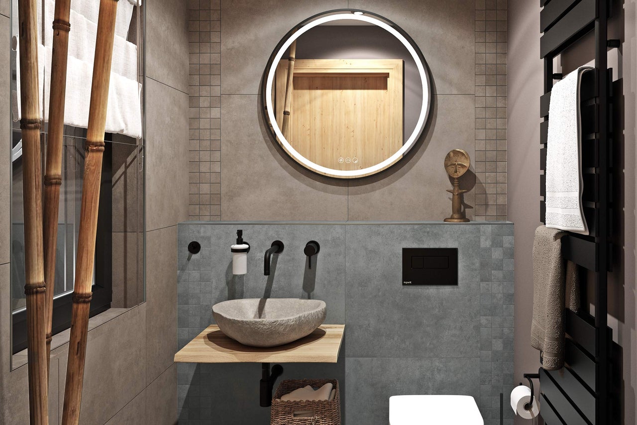 Moderne badkamer met ronde verlichte spiegel, natuurstenen opzetwastafel op houten console, zwarte wandkranen en grijze tegels.