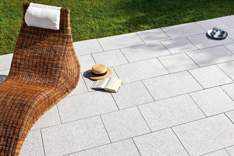 Tuinscene met rotan ligstoel, bestrating en zomeraccessoires