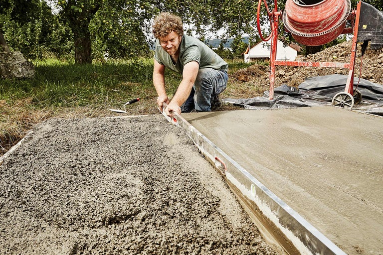 Man egaliseert beton met een waterpas, met een betonmolen op de achtergrond.