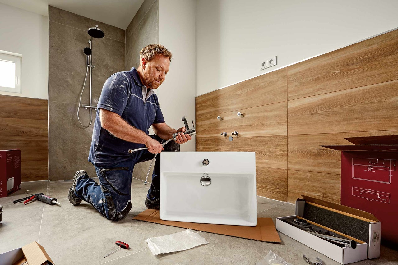 Een installateur installeert een wastafel in een badkamer met douche.