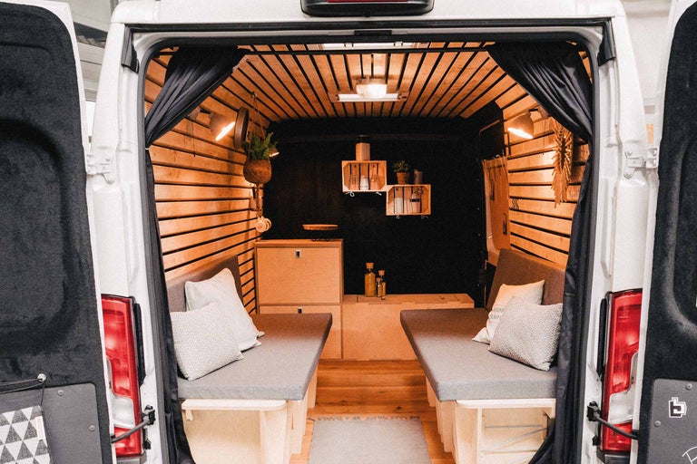 Interieur van een omgebouwde bestelwagen met houten lambrisering, bedden en een kitchenette.