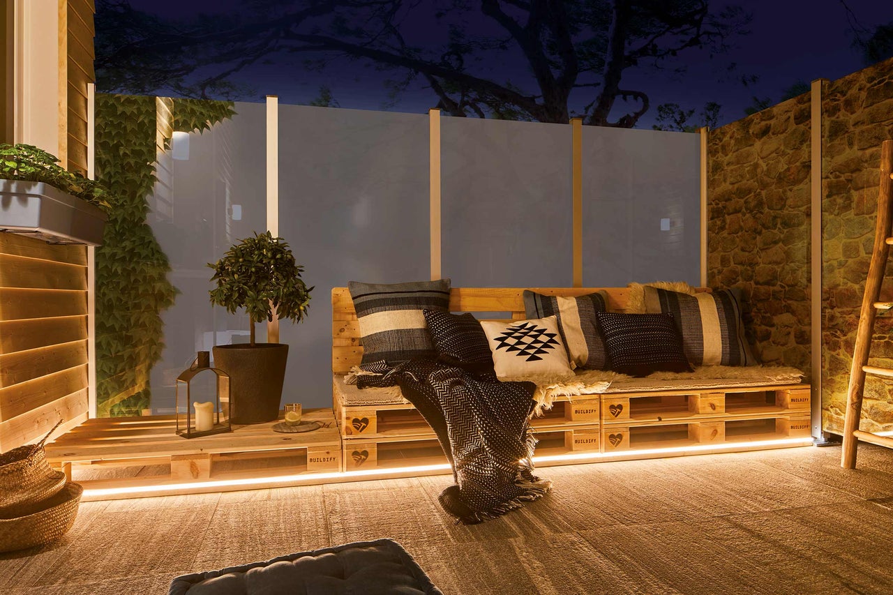 Aangelegde patio met houten meubels, planten en decoratieve verlichting voor een gezellige buitenruimte.