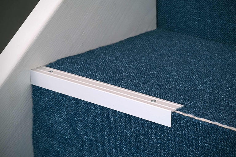 Detailopname van een trap met blauw tapijt en metalen trapkantprofiel