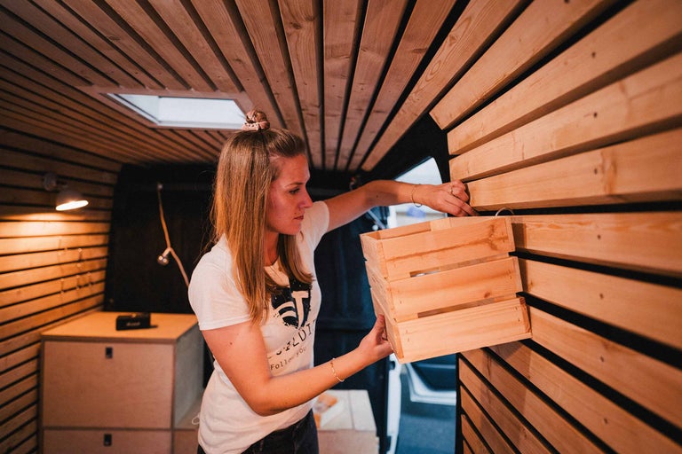 Vrouw monteert een houten kist aan een wand van houten panelen in een camper.