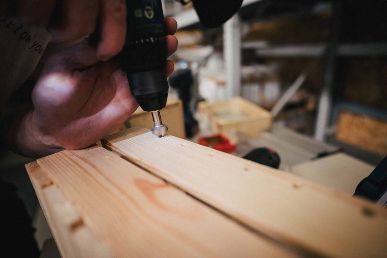 Een persoon gebruikt een boormachine om een gat in een houten plank te boren.