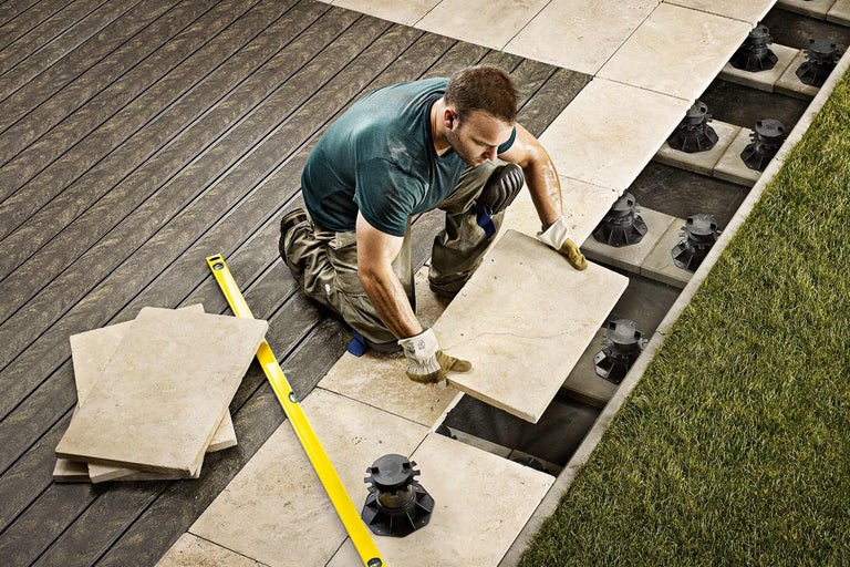 Een man legt stenen tegels op een terras met tegeldragers en een waterpas.