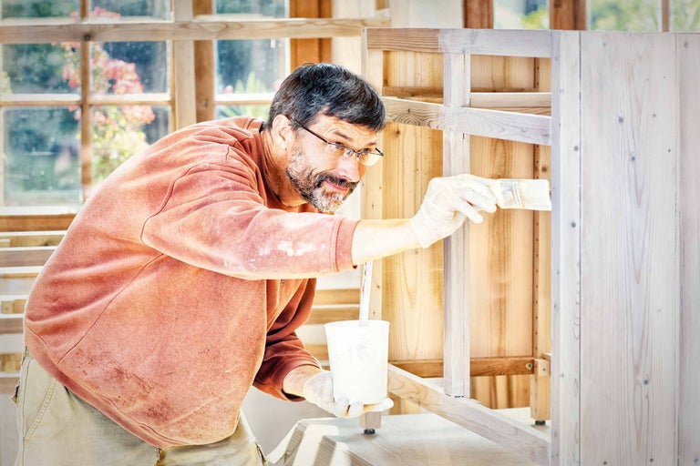 Een man schildert een houten kast met een kwast.