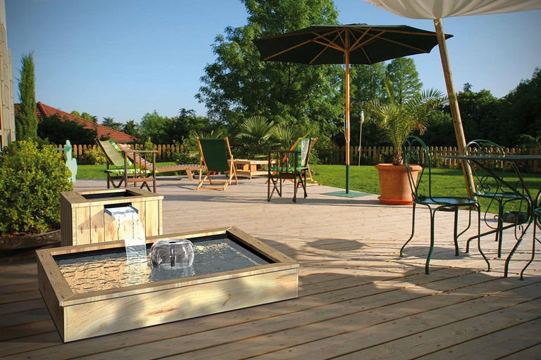 Tuinscene met houten waterspel, tuinmeubelen en parasols op een houten terras