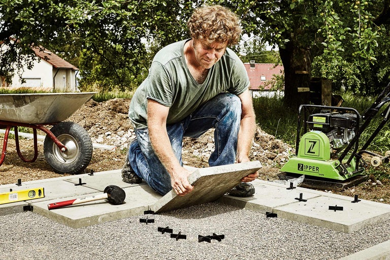 Man legt terrasplaten met een trilplaat, kruiwagen, rubberen hamer en waterpas in de tuin.