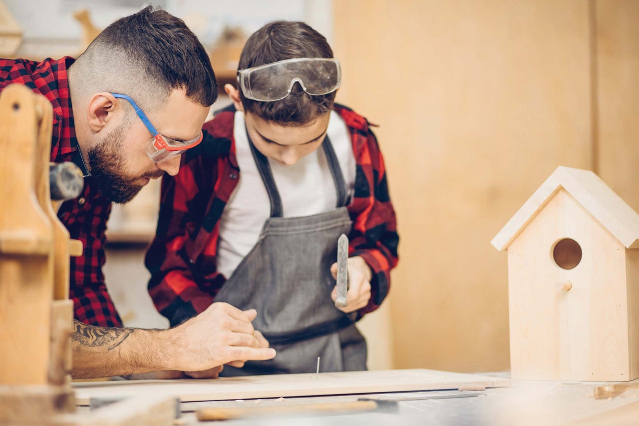 Vader en zoon bouwen samen een vogelhuis met hamer en spijker.