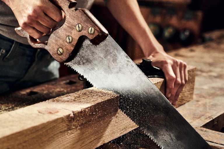 Een persoon zaagt een stuk hout met een handzaag.