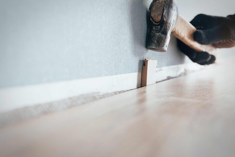 Een vakman bevestigt een plint met een hamer aan een muur.