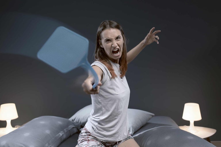 Vrouw met vliegenmepper in slaapkamer