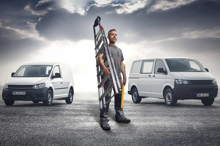 Vakman met ladder tussen twee bestelwagens