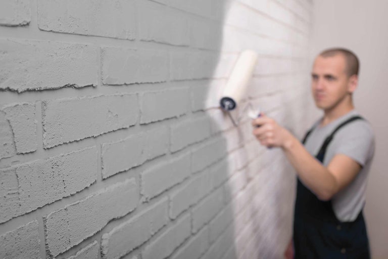 Man schildert een bakstenen muur met een verfroller