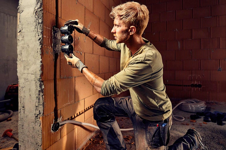 Elektricien installeert inbouwdozen in een bakstenen muur op een bouwplaats.
