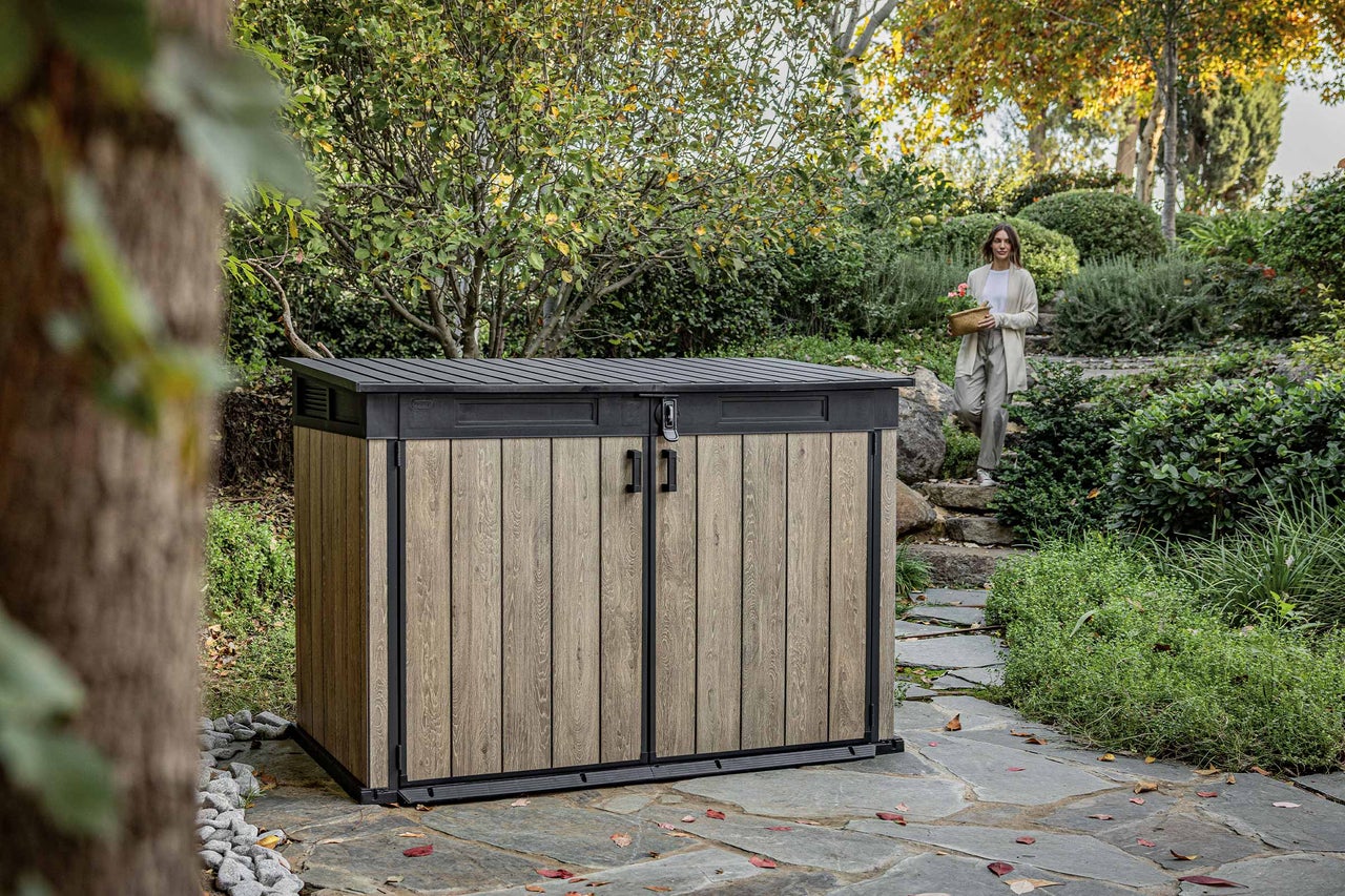 Tuinkast van hout en metaal in de tuin met een vrouw op de achtergrond