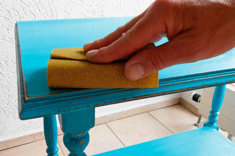 Een persoon schuurt een tafel met schuurpapier.