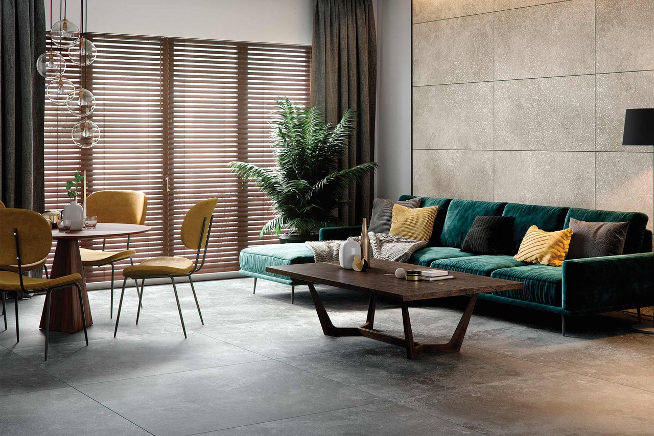 Woonkamer met bank, tafel, stoelen, vloertegels en jaloezieën