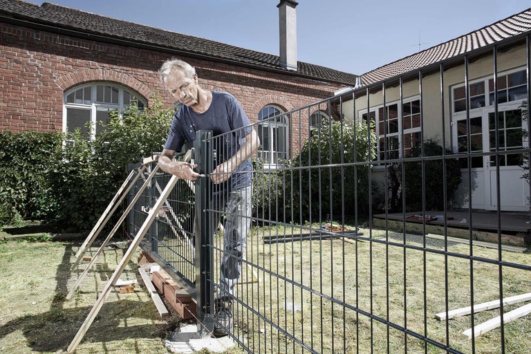 Man monteert een metalen hek in de tuin.