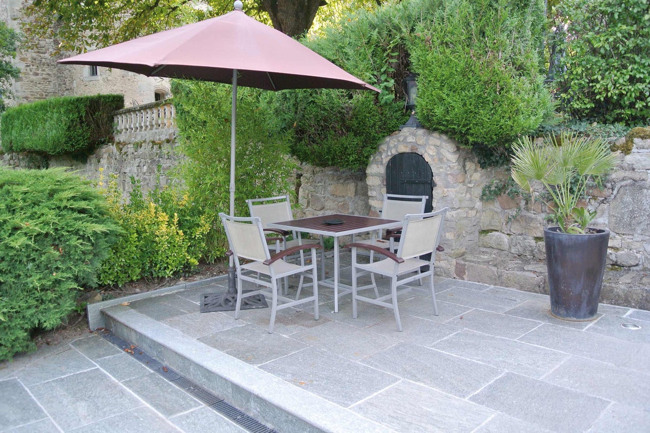 Vierkante tuintafel met vier stoelen en parasol op een betegeld terras