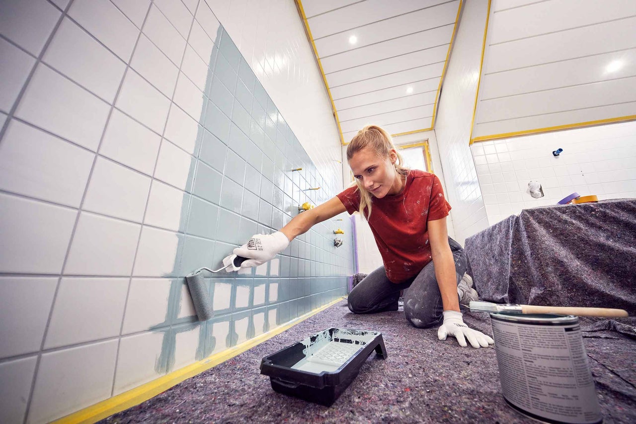 Een persoon schildert tegels met een verfroller.