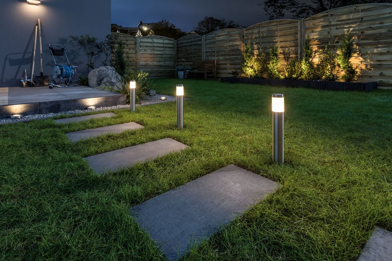 Verlichte tuin met gazon, pad van stenen platen en tuinlampen