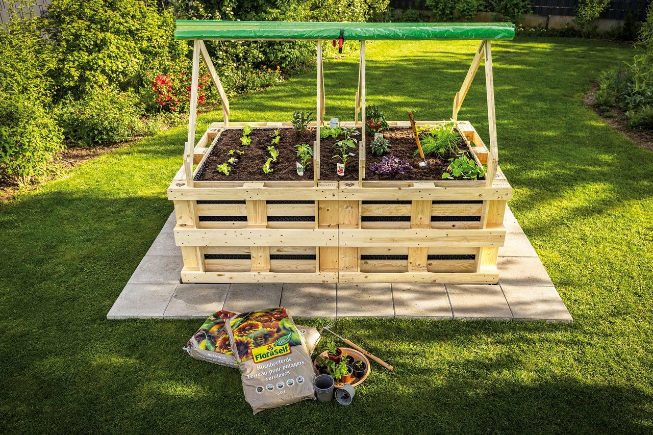 Houten verhoogde tuinbak met planten en groenten in de tuin, met potgrond op de voorgrond.