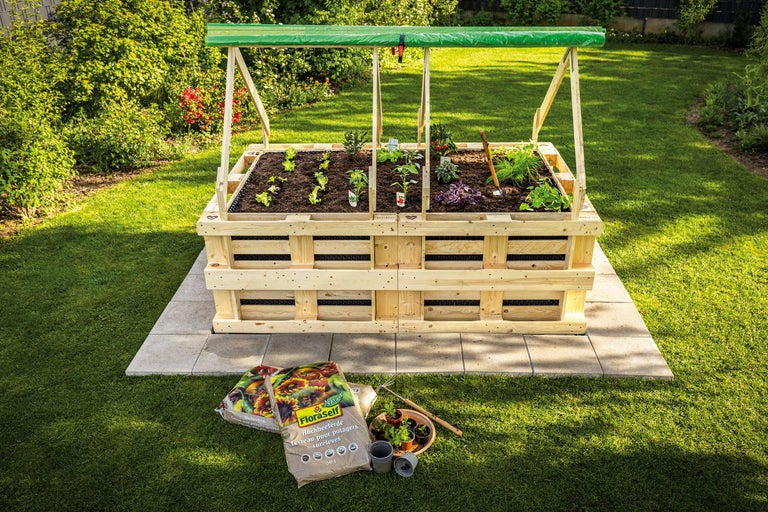 Houten verhoogde tuinbak met planten en groenten in de tuin, met potgrond op de voorgrond.