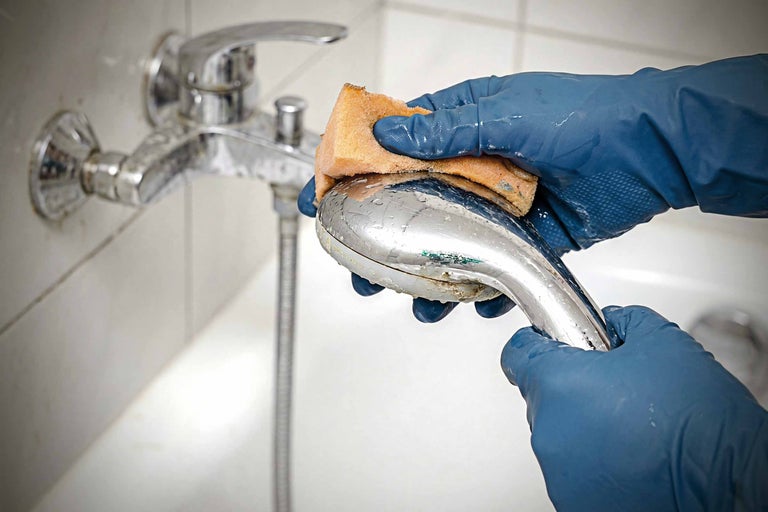 Een persoon met beschermende handschoenen maakt een douchearmatuur schoon met een spons.