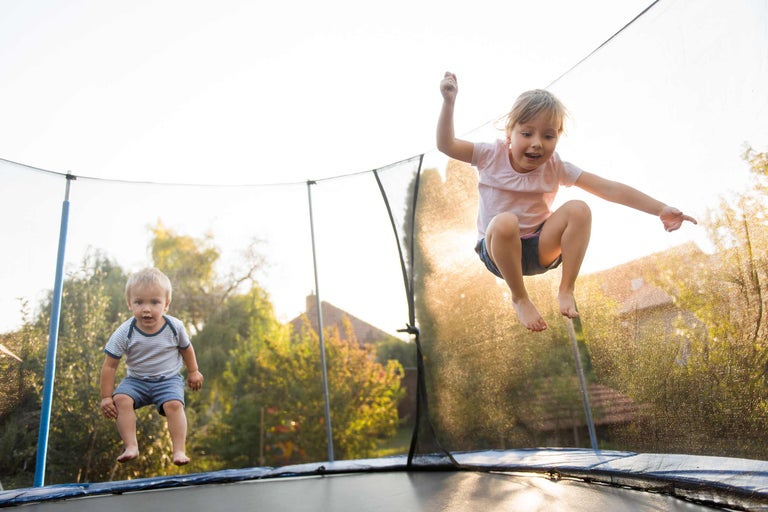 Twee kinderen springen op een tuintrampoline met veiligheidsnet.